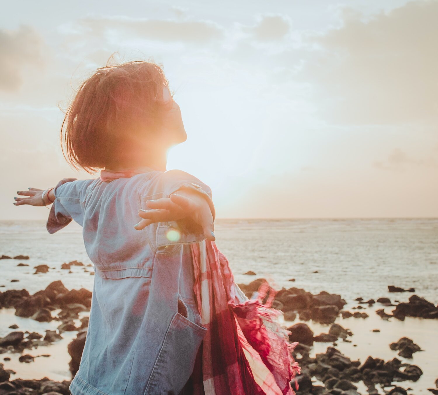 a woman with open arms looking towards the sunset