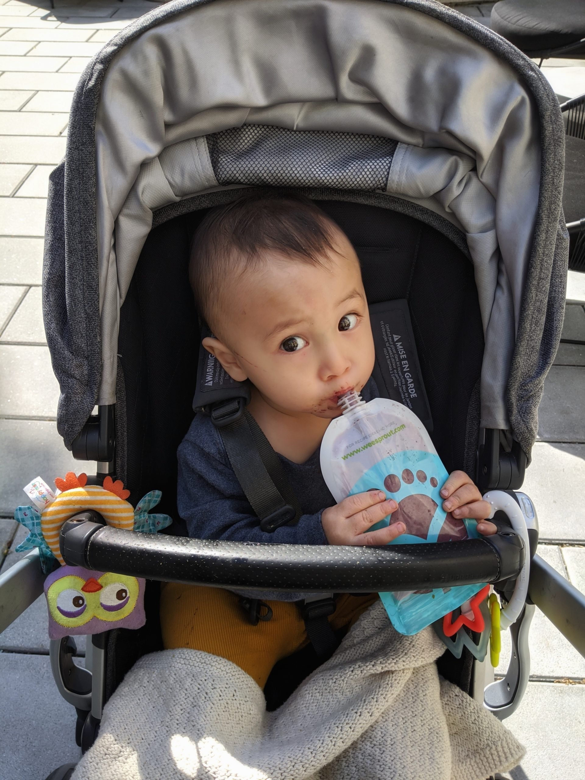 Baby in stroller eating from a smoothie pouch