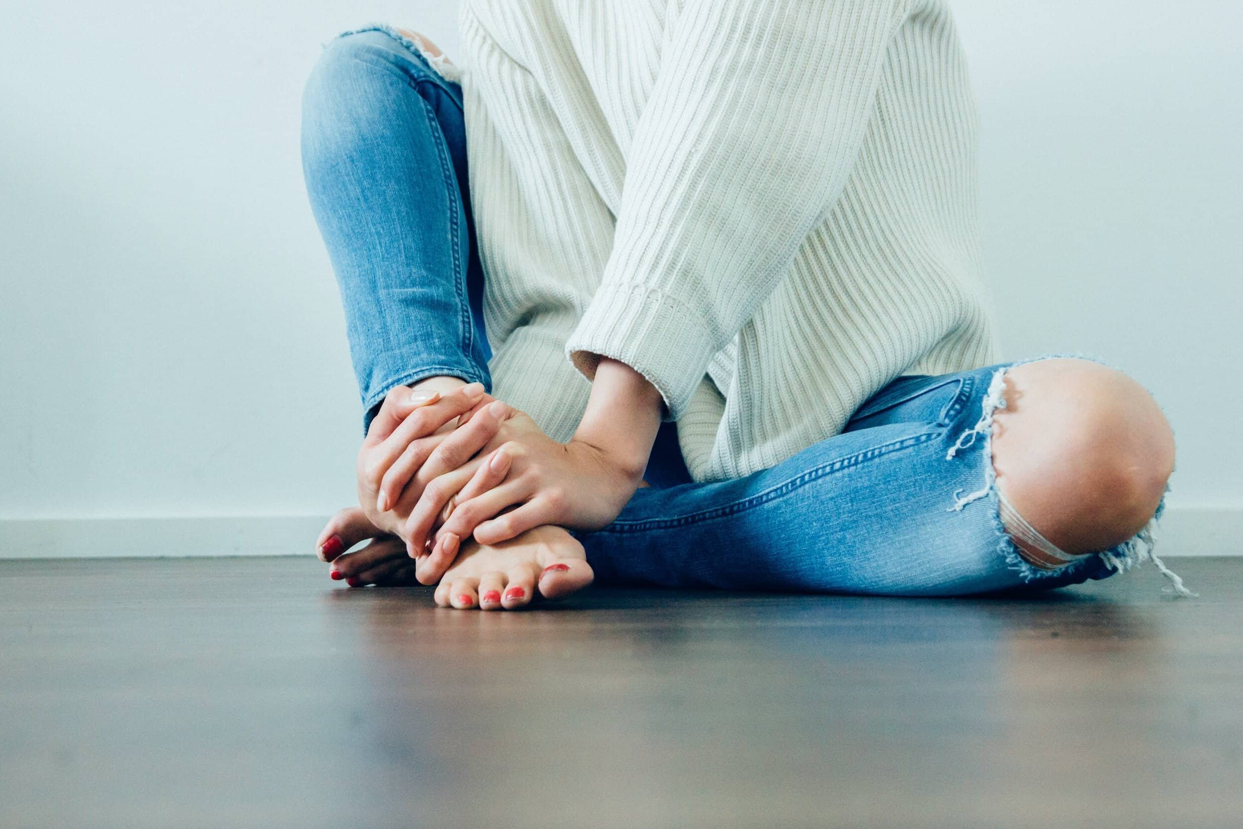 Woman sitting in ripped jeans, touching feet.