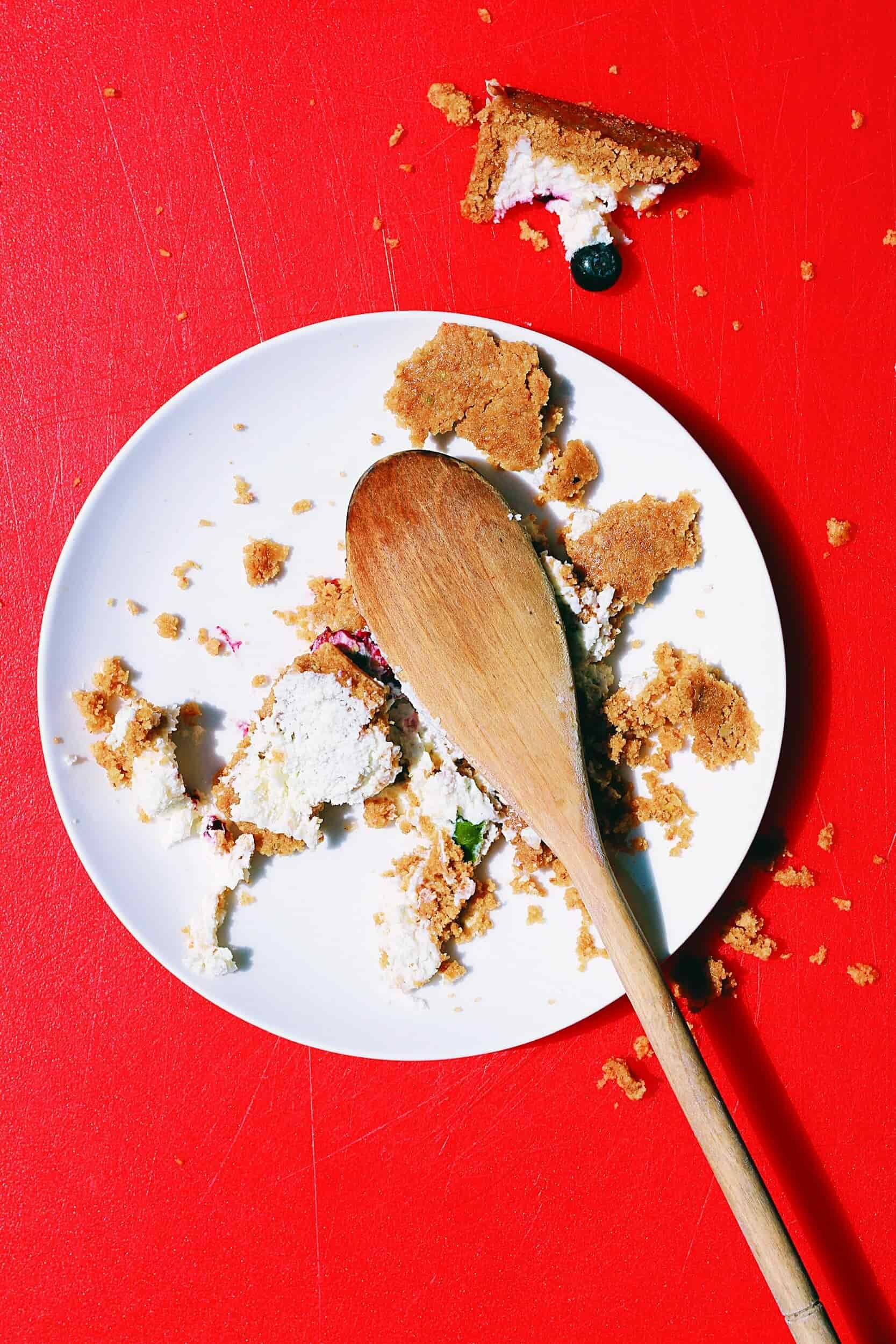 A half eaten, crumbled dessert with blueberries with wooden spoon on the plate.