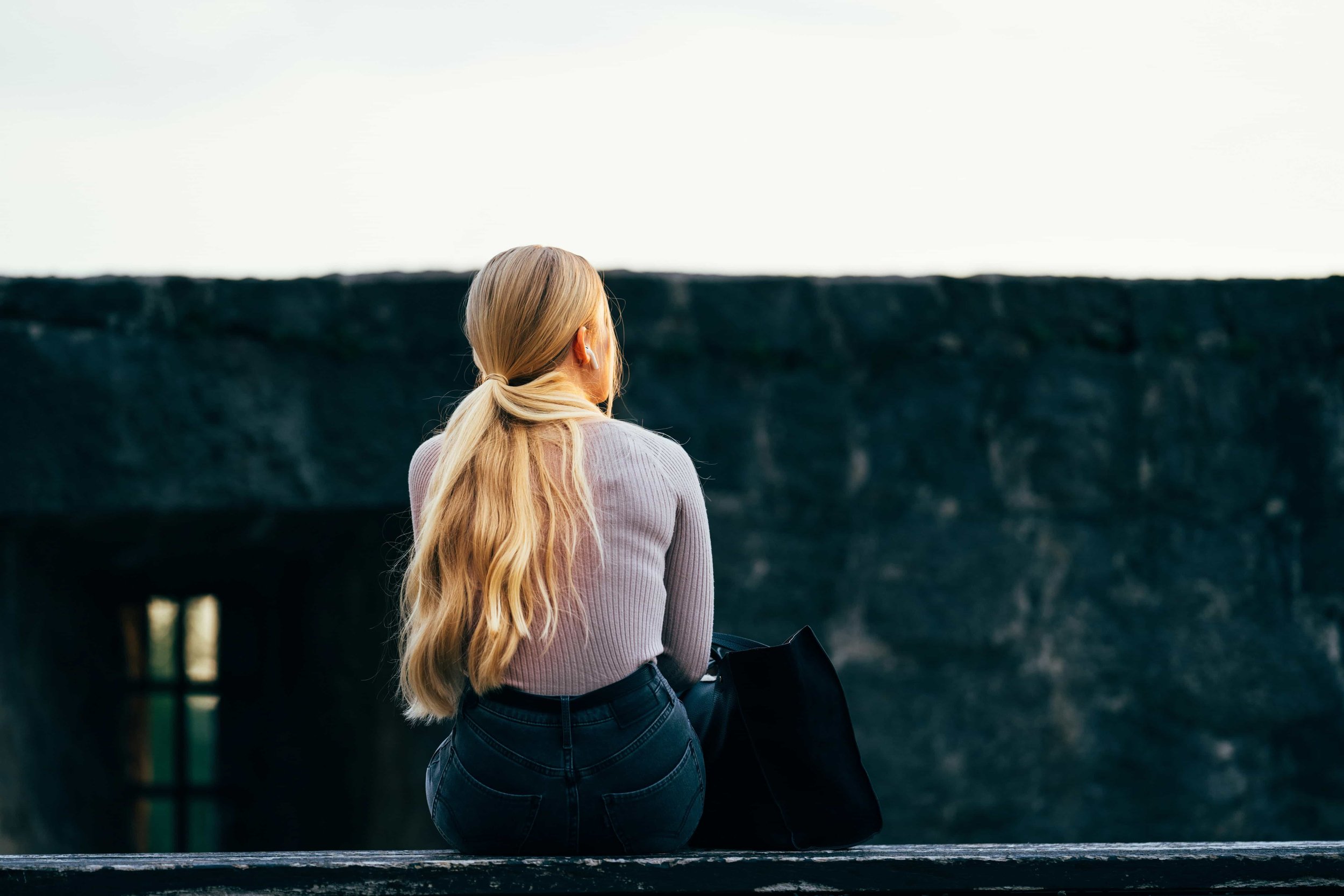 Woman sitting on a rooftop. Her purse next to her. View from her back.