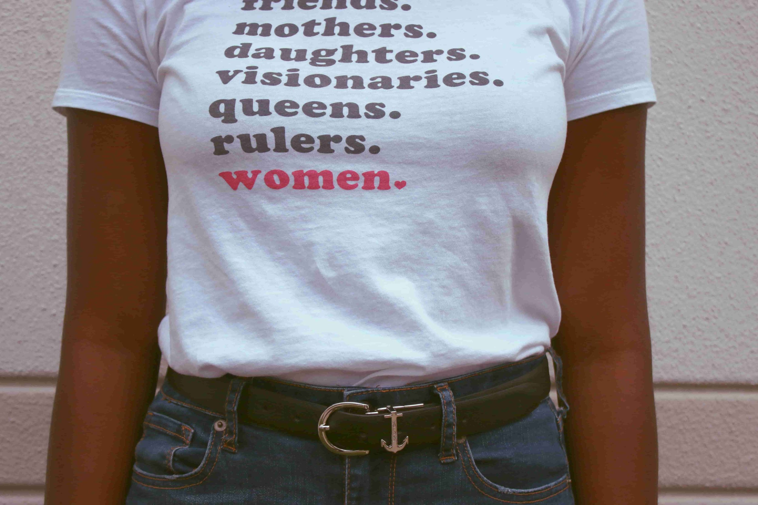 A woman wearing a shirt that says friends. mothers. daughters. visionaries. queens. rulers. women.