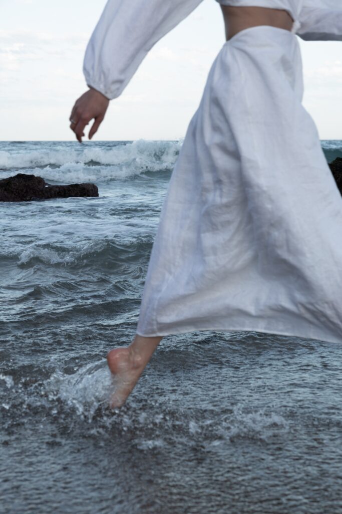 Dusk - Person in white linen wading through ocean waves - TVS