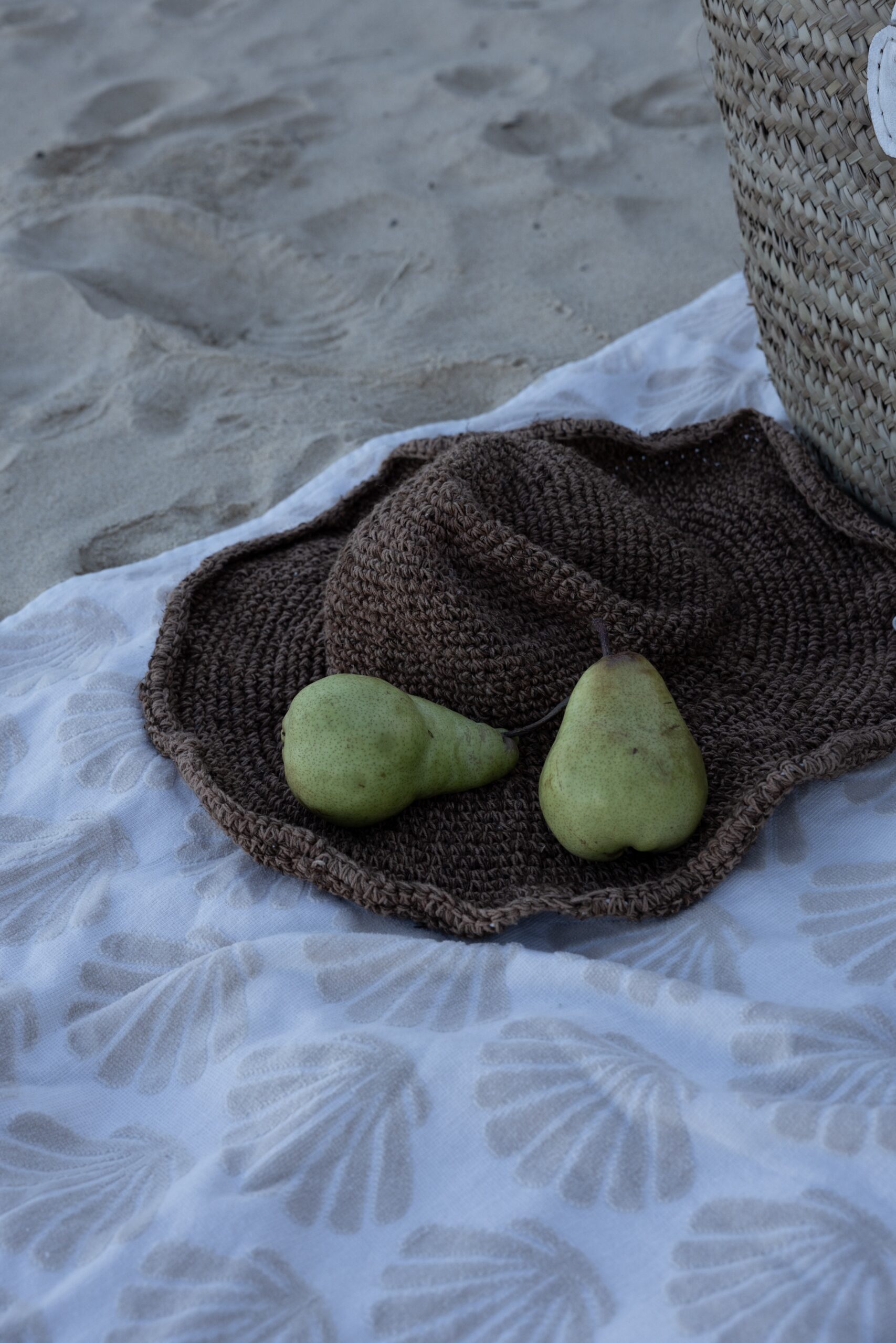 Two green pears in woven basket on sandy beach