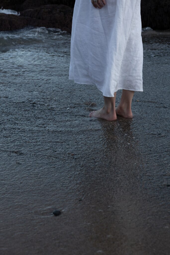 Woman in a white dress wading through shallow ocean water.