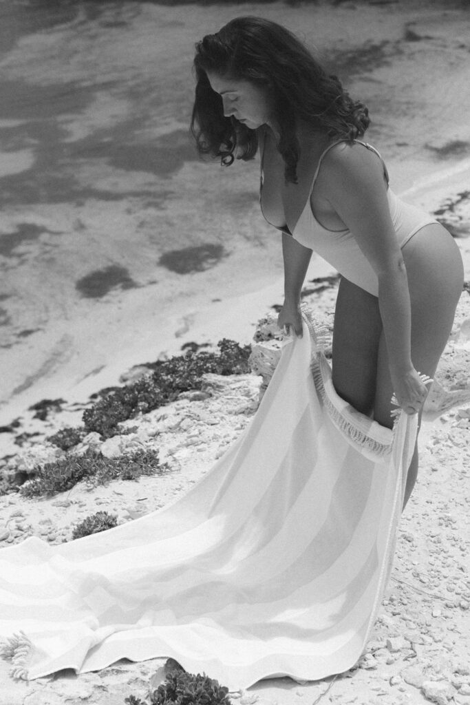 Black and white photo of a woman laying her beach towel on the shore.