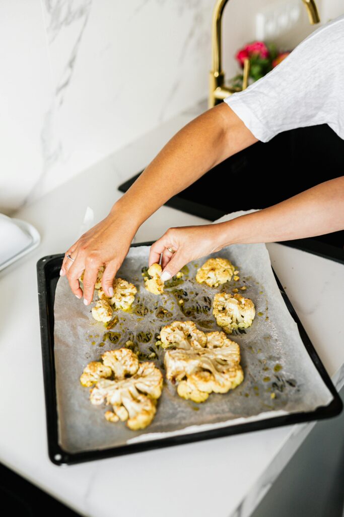 two hands laying cauliflowers on a baking tray