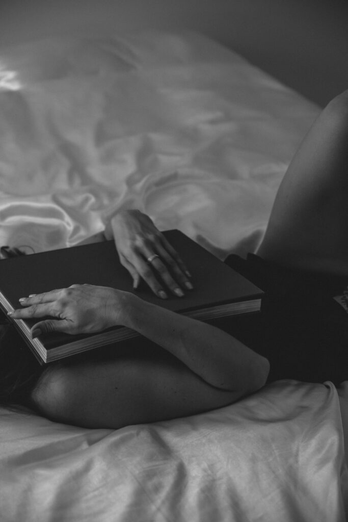 A person reclines on a bed, holding a book close. The soft light highlights their relaxed pose and peaceful atmosphere, evoking a sense of calm and contemplation.