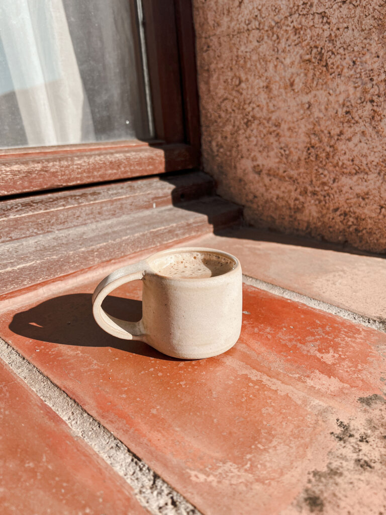 Warm drink in a minimalist white ceramic cup, placed on terracota. Every daily act can become a spiritual practice. 