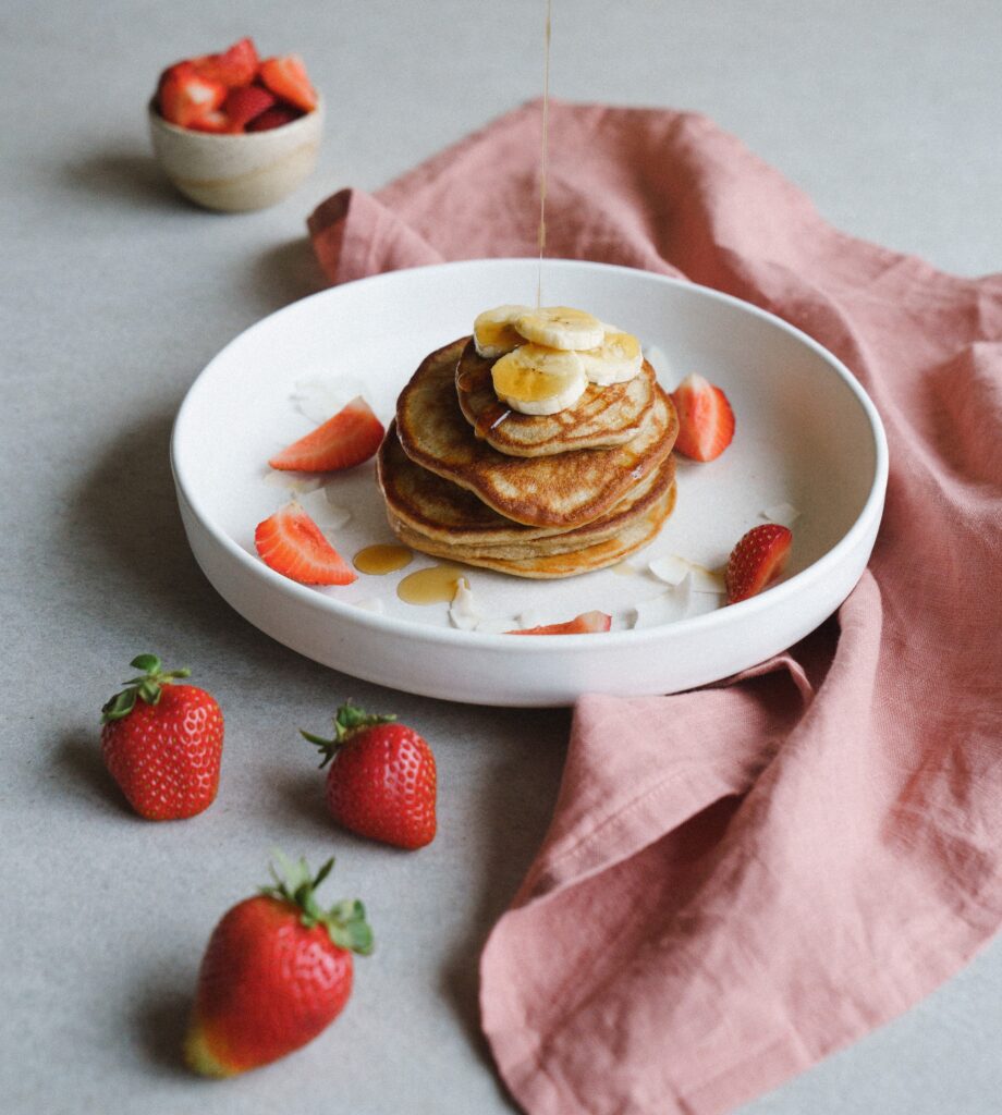 Stack of pancakes served with bananas and sliced strawberries