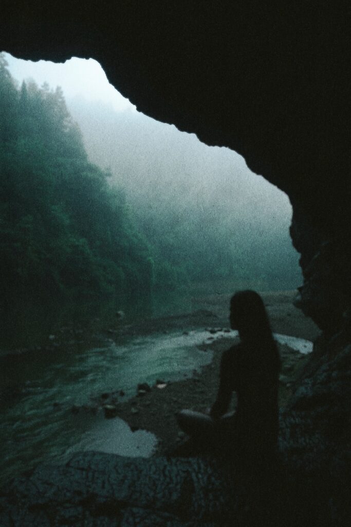 Silhouetted figure gazing out from misty forest cave opening