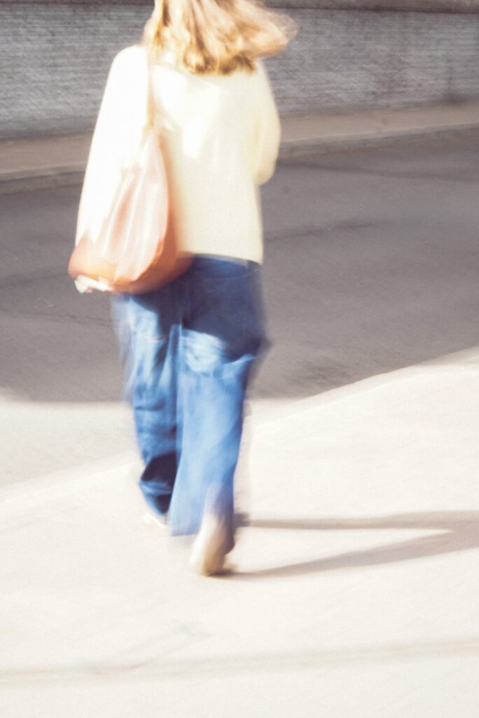 Woman in casual outfit walking on sunny pavement
