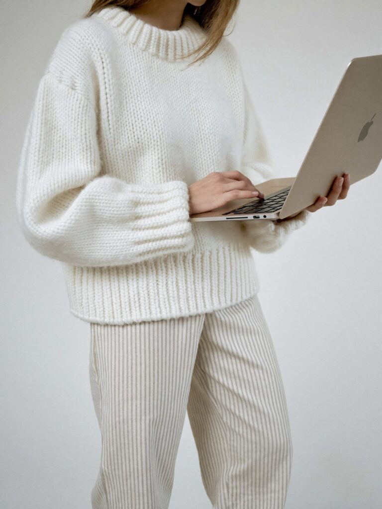 Woman in cream knit set working on laptop 