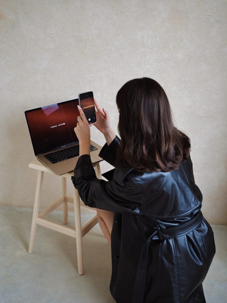 Woman photographing laptop screen with smartphone
