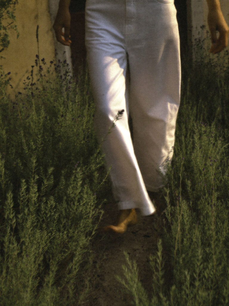 Person in white wide-leg trousers walking barefoot through tall green grass. Nature can be medicine for your nervous system health