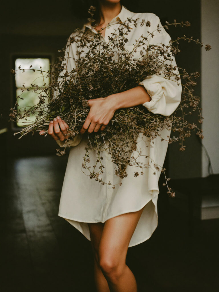 Woman-in-oversized-white-shirt-dress-holding-large-bundle-of-dried-wildflowers
