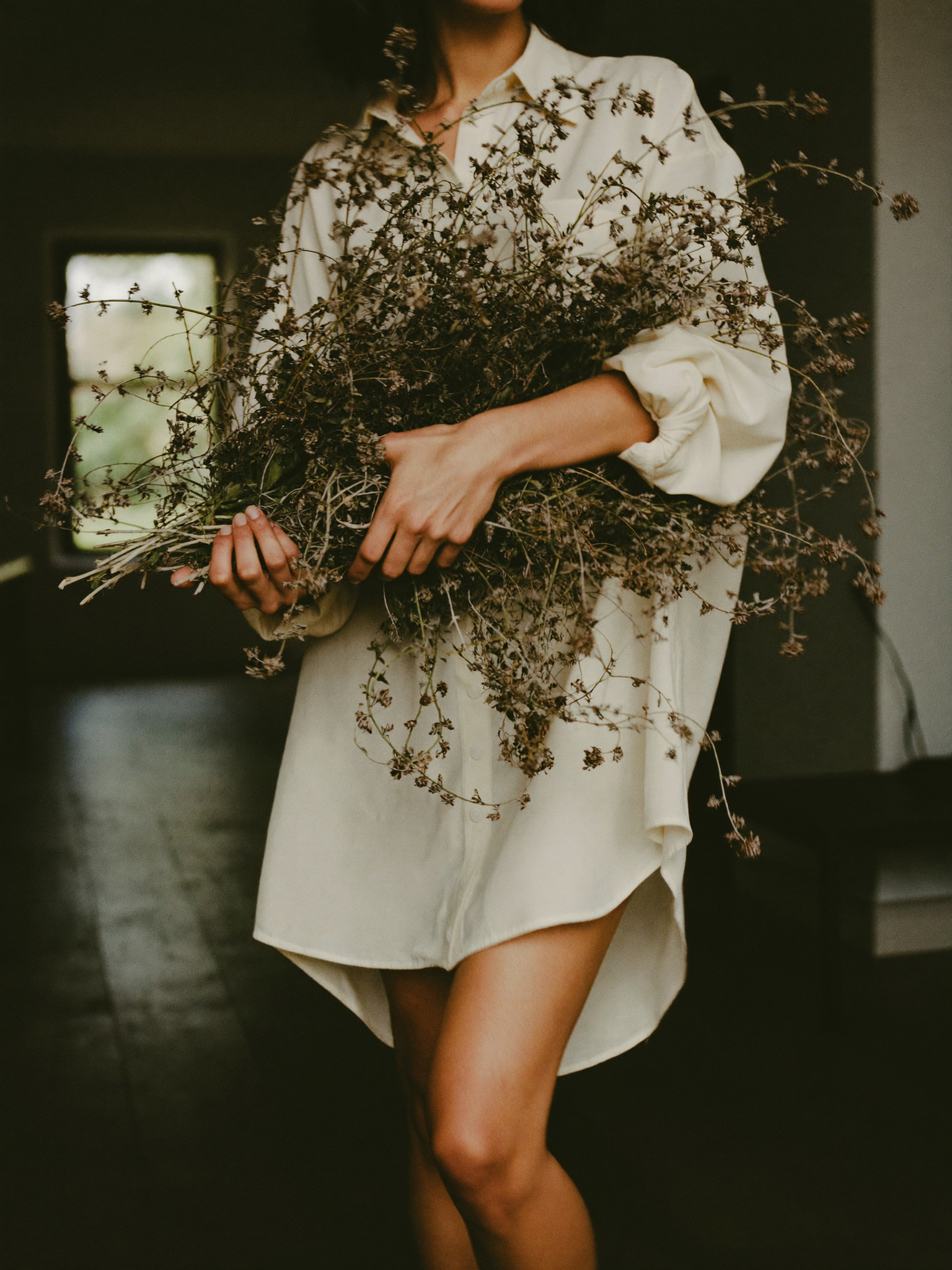 Woman-in-oversized-white-shirt-dress-holding-large-bundle-of-dried-wildflowers